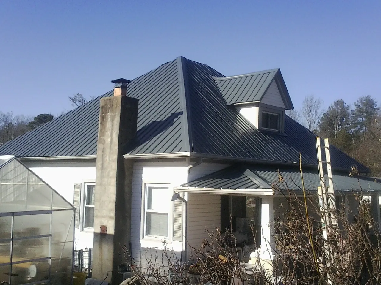 Dark blue standing seam metal roof on a white farmhouse with dormer — Slate & Tile Roof Repair by Roofing Brothers in Calhoun City
