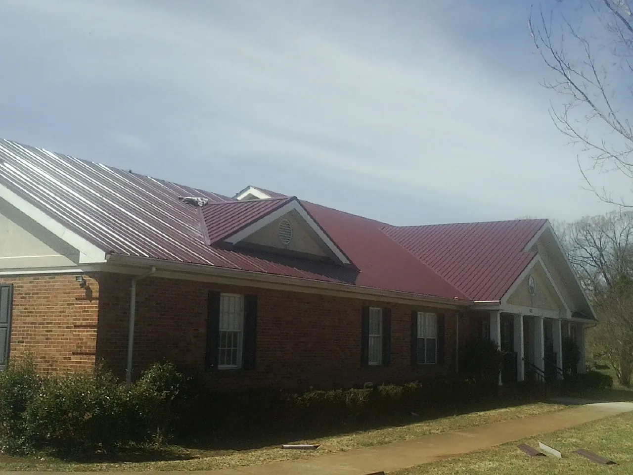 Red metal roof with gabled entries on a long brick building, from a Hail Damage Roof Repair job in Calhoun City
