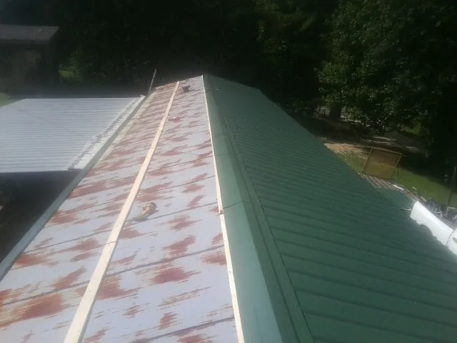 Old rusted panels beside newly installed green metal roofing — Wind Damage Roof Repair by Roofing Brothers in Calhoun City