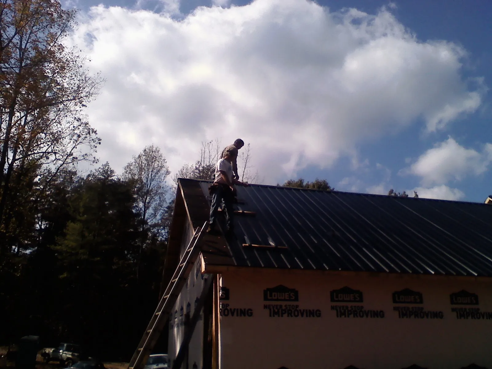 Roofer fastening dark metal panels high against a cloudy sky, from a Roof Inspection job in Calhoun City