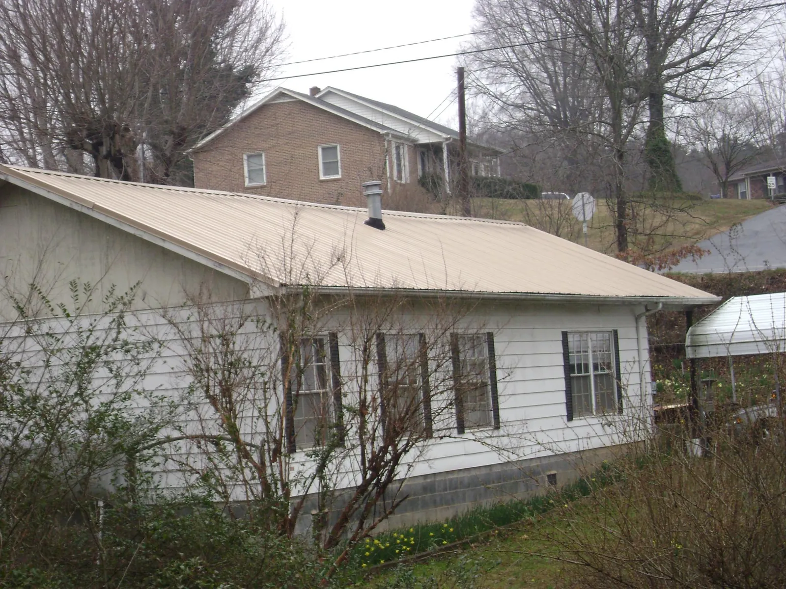 Tan metal roof on a white sided house set into a hillside — Commercial Roofing by Roofing Brothers in Calhoun City